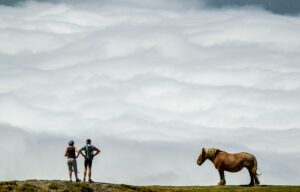 Photo by <a href="https://unsplash.com/@martinbennie?utm_content=creditCopyText&utm_medium=referral&utm_source=unsplash">martin bennie</a> on <a href="https://unsplash.com/photos/a-couple-of-people-stand-near-a-horse--1qa0PFVKxs?utm_content=creditCopyText&utm_medium=referral&utm_source=unsplash">Unsplash</a> Two people chatting in the open air on a hill overlooking clouds near a sturdy looking hill